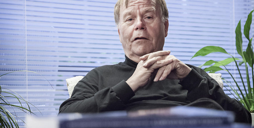 Juhani Laurinkari istuu olohuoneessa, sohvapöydällä kirjapino.