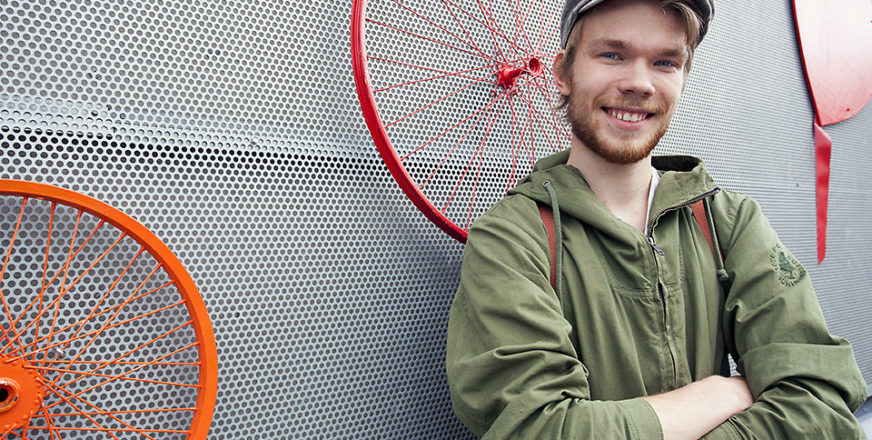 Elias Kvisti nojaa torilla seinään, jota koristaa värikkäät pyöränvanteet.