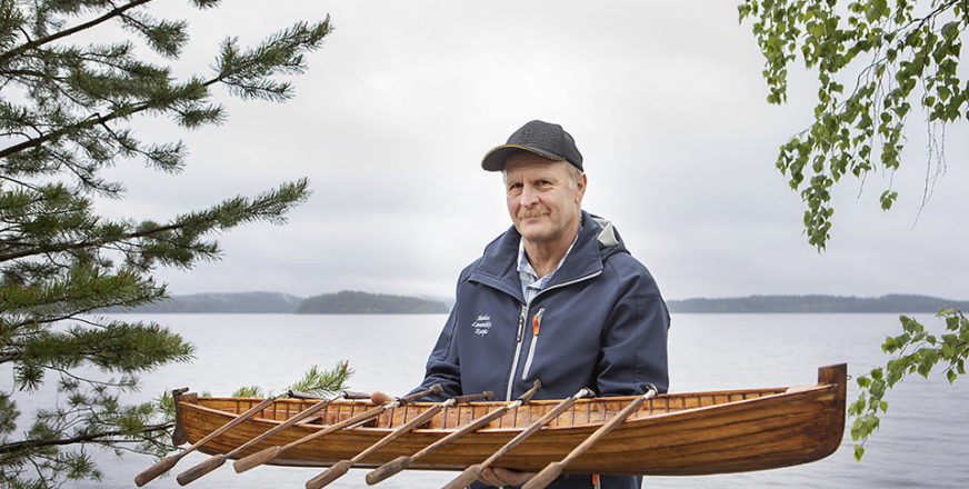 Jorma Konttinen, joka pitää käsissään rakentamaansa kirkkoveneen pienoismallia. Taustalla näkyy järvi.