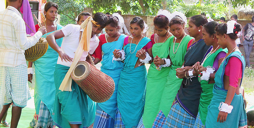 Nepalilaisia naisia värikkäissä asusteissa, kaksi nuorta miestä soittaa rumpuja naisten edessä.