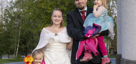 Nina Bredenberg ja Mika Pöyhönen seisovat lapsineen ulkona kirkon pihalla juhlapuvut yllään..