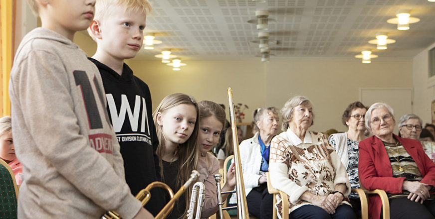 Kalevalan koulun 5A-musiikkiluokan oppilaat Matti Kärkkäinen, Topi Toivanen, Alma Tiitinen ja Terhi Koskenvuori seisovat soittimineen vanhusten vieressä Männistön palvelutalolla.