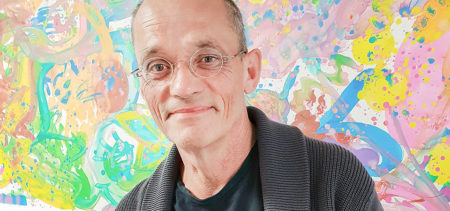 Puolivartalokuva Tommi Auvisesta pastellisävyisen maalauksen edessä