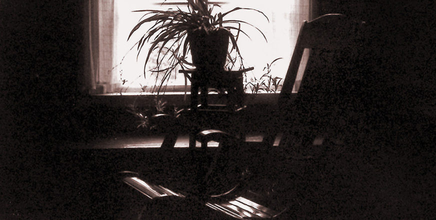 Tummanpuhuvassa kuvassa tupa, jossa ikkunan edessä tyhjä keinutuoli.