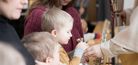 Pieni poika ehtoollisella, pappi tarjoaa ehtoollisiviiniä.