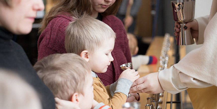 Pieni poika ehtoollisella, pappi tarjoaa ehtoollisiviiniä.