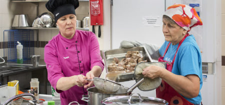 Kaksi naista valmistaa ruokaa suurtalouskeittiössä.