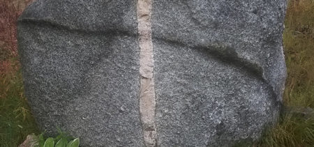 Iso harmaa kivi, johon erivärinen pystyraita ja vaakasuuntainen raita muodostavat ristin.