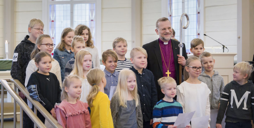 Piispa Jari Jolkkonen ympärillään lapsikuoro Valonsäteen laulajat.