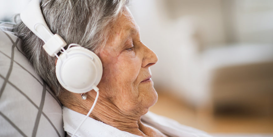 Vanhus kuuntelee kuulokkeet korvillaan musiikkia silmät kiinni makuullaan.