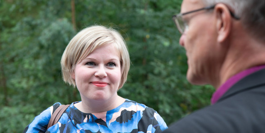 Annika Saarikko ja hänen edessään mies, jolla violetti paidankaulus kuin piispalla.