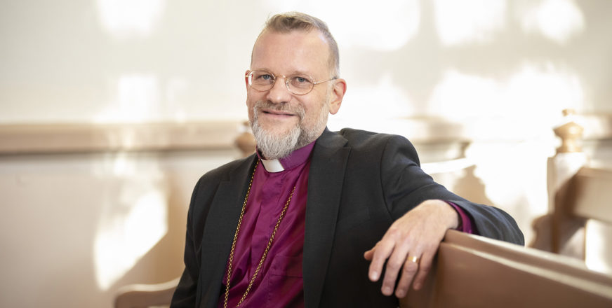 Piispa Jari Jolkkonen istuu kirkon penkillä.
