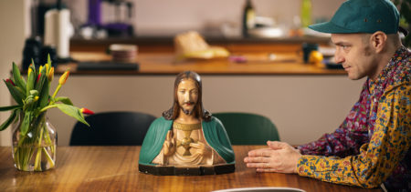 Jaakko Kämäräinen istuu sivuttain pöydän päässä ja katselee pöydällä olevaa Jeesus-patsasta