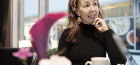 Johanna Elola istuu kahvilassa kahvikupin ääressä värikkään kukka-asetelman takana.