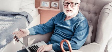 Harmaapartainen mies istuu nojatuolissa, sylissä kannettava tietokone.
