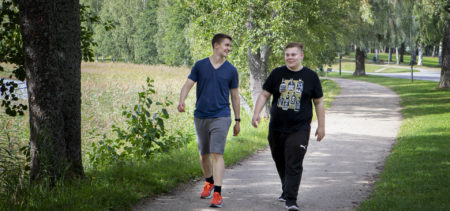 Kaksi nuorta aikuista kävelee puistotiellä.