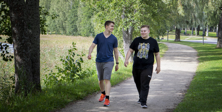 Kaksi nuorta aikuista kävelee puistotiellä.