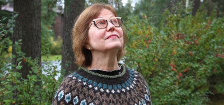 Raija Kilpeläinen-Somero katsoo kohti taivasta, taustalla metsää