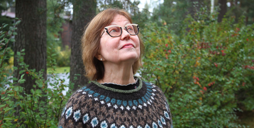 Raija Kilpeläinen-Somero katsoo kohti taivasta, taustalla metsää