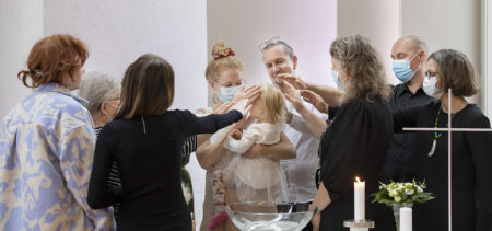 Läheiset siunaavat kastetun lapsenpapin kanssa laittamalla kädet kastetun pään päälle.