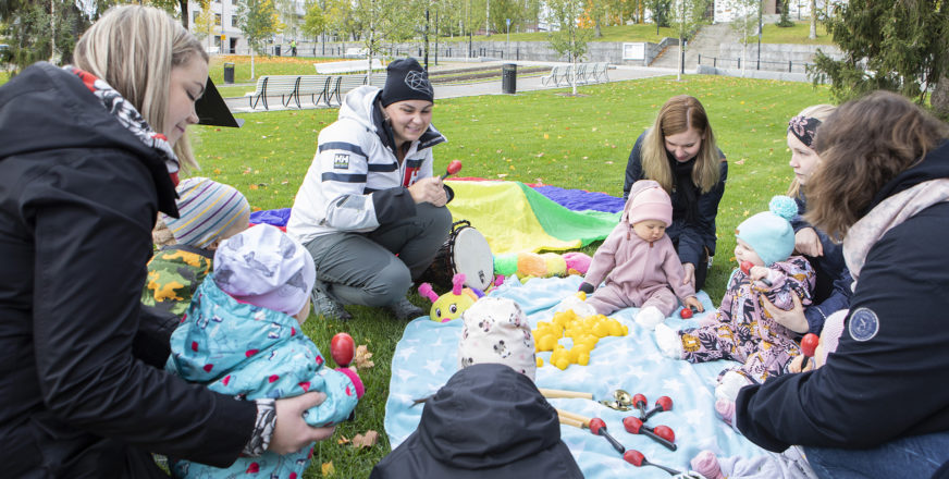 Aikuisia ja vauvoja nurmikolle levitetyn viltin ääressä.