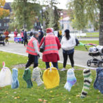 Etualalla pieniä villasukkia narulla, taka-alalla ihmisiä ja lastenvaunuja puistossa.