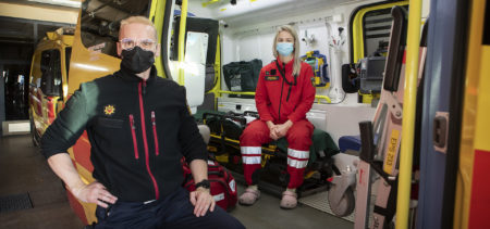 Pelastaja seisoo ambulanssin vieressä, ensihoitaja istuu ambulanssin sisällä.