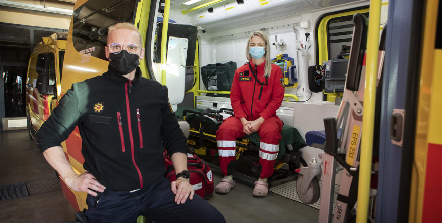 Pelastaja seisoo ambulanssin vieressä, ensihoitaja istuu ambulanssin sisällä.