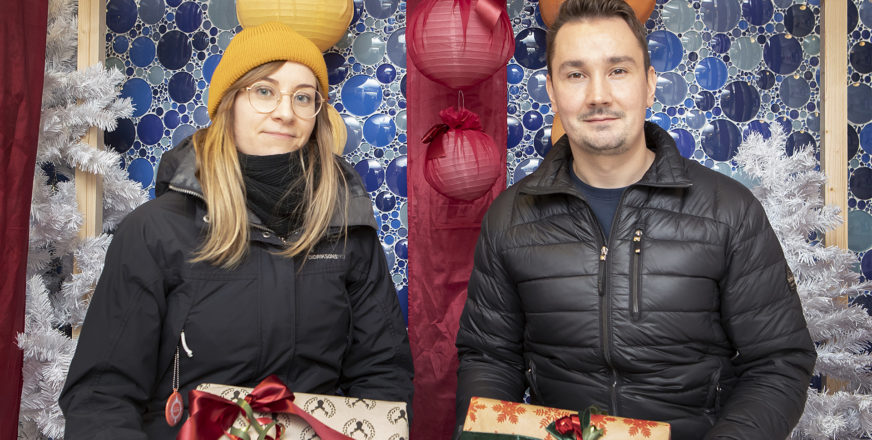 Nainen ja mies istuvat ulkovaatteisiin pukeutuneina lahjapaketit käsissään.
