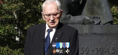 Väinö Rissanen tummassa puvussa ja kunniamerkit rinnassaan sankarivainajien muistomerkin edessä