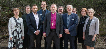 Piispa ja 9 muuta ihmistä yhteiskuvassa pihamaalla.