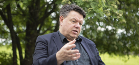 Petteri Taalas istumassa ulkona taustallaan kesäistä luontoa.