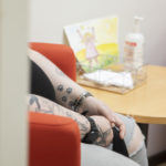 Ihminen istuu punaisessa nojatuolissa, tatuoidut kädet, taustalla piirroskuva pöydällä.