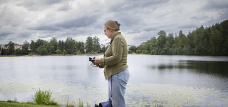 Diakoniatyöntekijä Kati Ukkonen selaa puhelinta lammen rannalla.