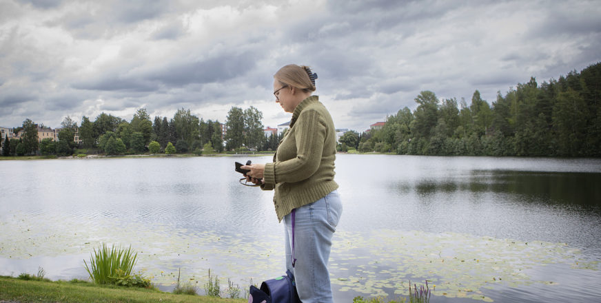 Diakoniatyöntekijä Kati Ukkonen selaa puhelinta lammen rannalla.