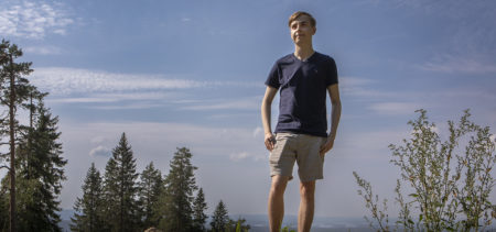 Hugo Korhonen seisomassa Puijon laella, taustalla puita ja paljon sinistä taivasta