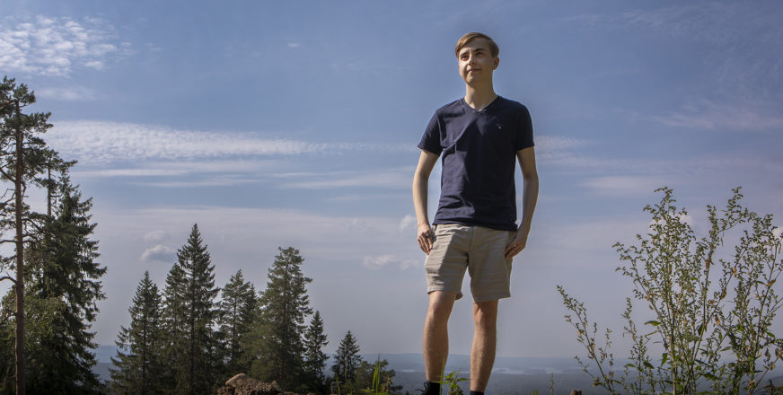 Hugo Korhonen seisomassa Puijon laella, taustalla puita ja paljon sinistä taivasta