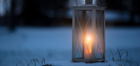 Lyhty, jossa palaa kynttilä. Taustalla luminen maisema.