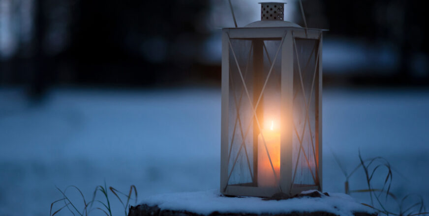 Lyhty, jossa palaa kynttilä. Taustalla luminen maisema.