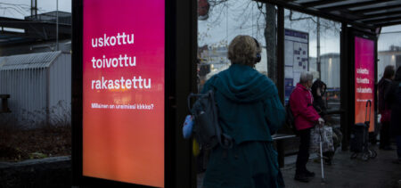 Bussipysäkillä seurakuntavaalien mainos, ihmisiä.