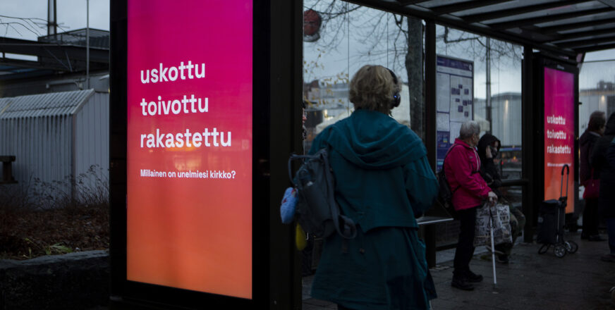 Bussipysäkillä seurakuntavaalien mainos, ihmisiä.