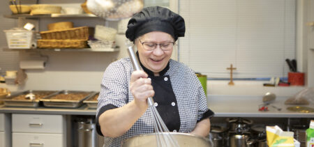 Emäntä sekoittaa makaronilaatikon lientä hymyilevänä.