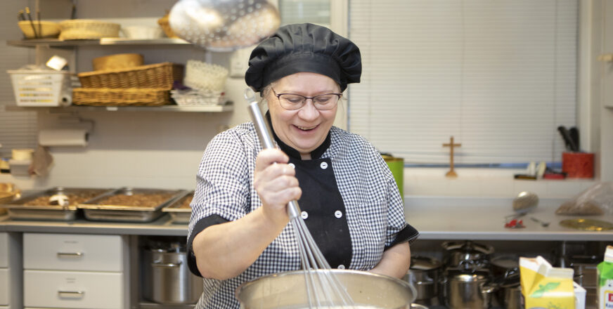 Emäntä sekoittaa makaronilaatikon lientä hymyilevänä.