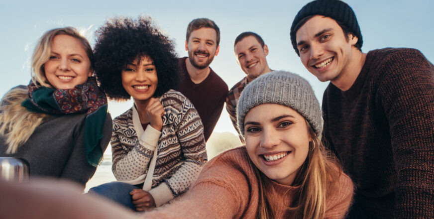 Kuusi nuorta aikuista, joista etummainen ottaa ryhmästä selfiekuvaa.