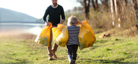 Aikuinen ja lapsi kantavat täysiä roskapusseja rannalla.