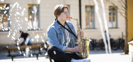 Onni Yläkorhola istuu ulkona soittamassa saksofonia.