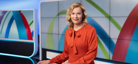 Uutisankkuri Piia Pasanen punaisessa asussa pöydän ääressä tv-studiossa