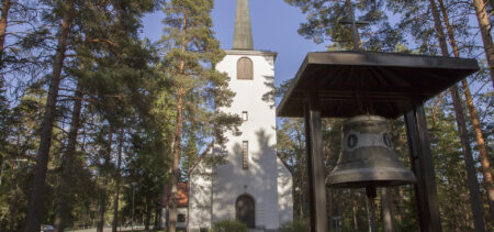 Riistaveden kirkko ja kellotorni puiden keskellä kesällä.