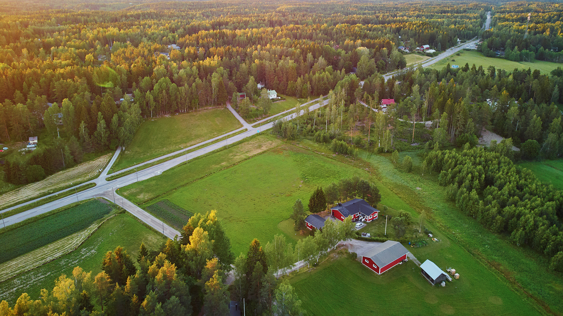 Ilmakuva maaseudulta. Talo, metsää , nurmikenttää ja kuvaa halkova maantie