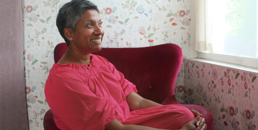 Anu-Rohima Mylläri istuu nojatuolissa hymyillen ja katsoo kohti ikkunaa poispäin kamerasta